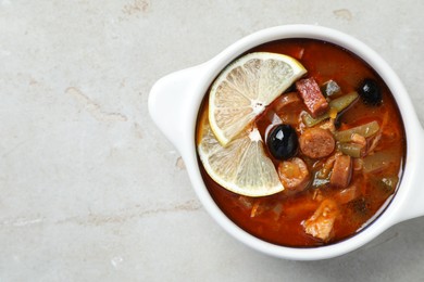 Photo of Meat solyanka soup with sausages, olives and vegetables in bowl on white textured table, top view. Space for text