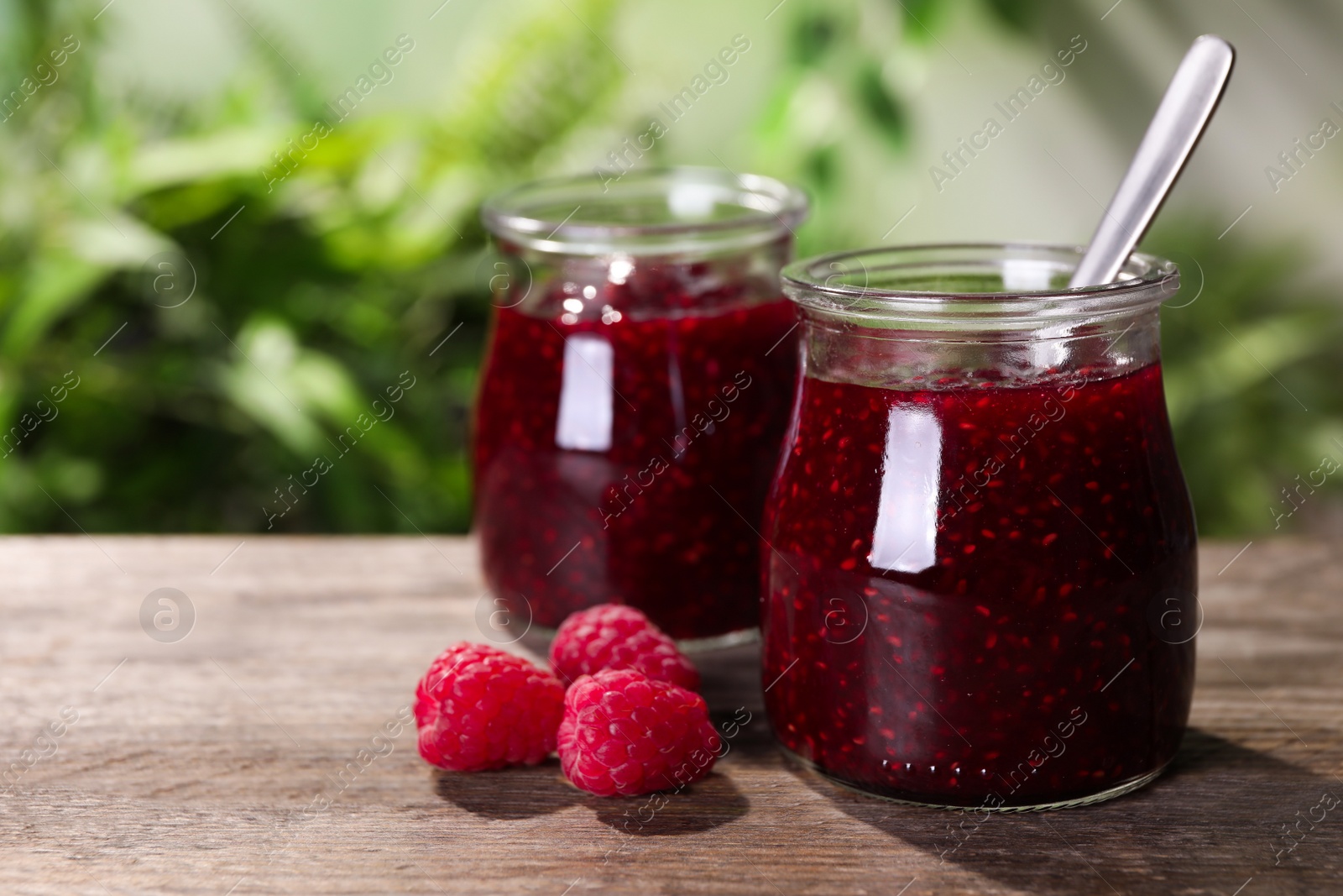 Photo of Delicious jam and fresh raspberries on wooden table