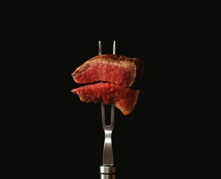 Photo of Carving fork with pieces of steak on black background. Tasty meat