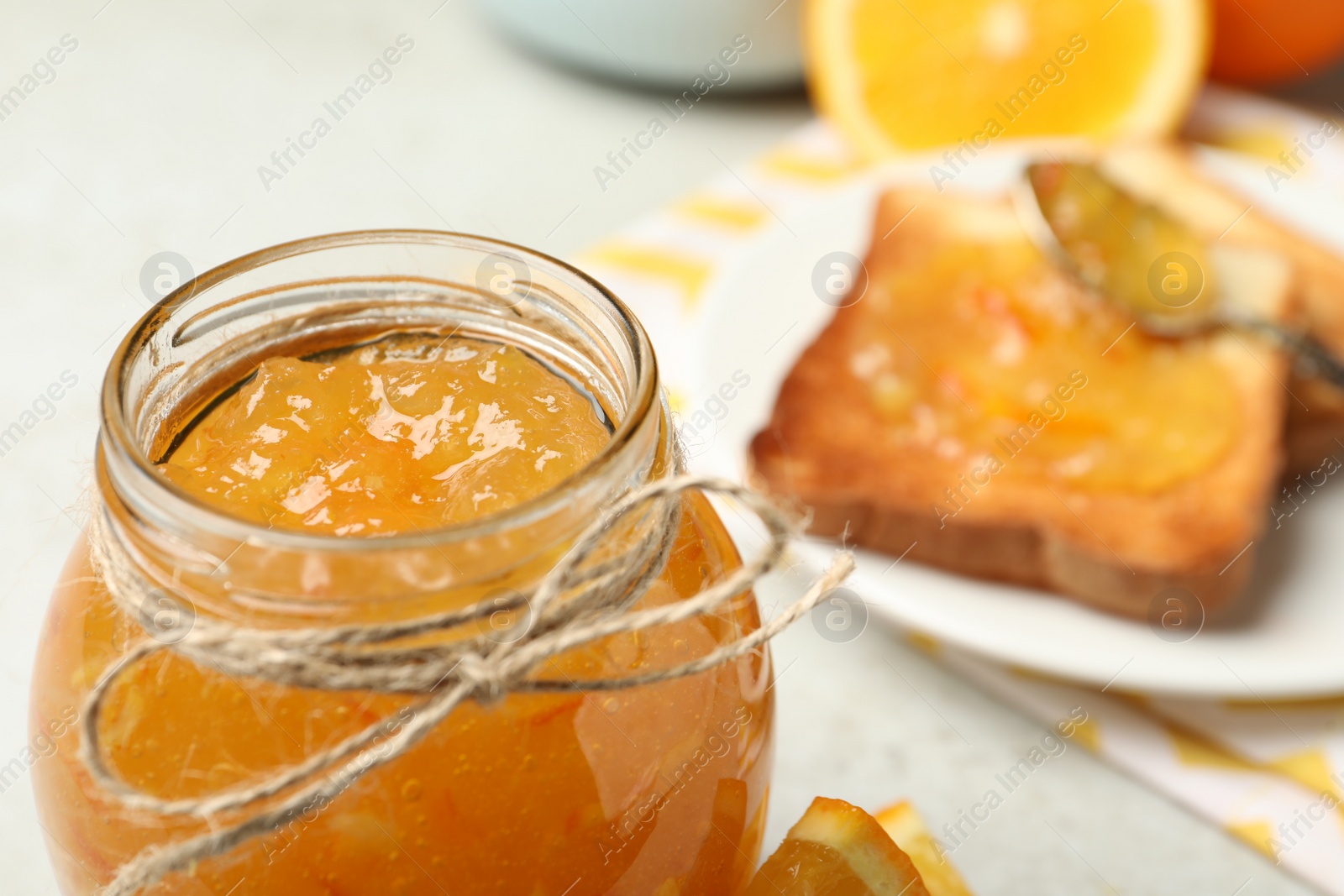 Photo of Delicious orange marmalade in glass jar on light table, closeup. Space for text
