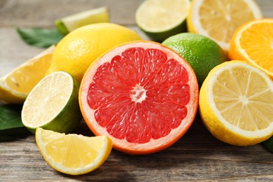 Different fresh citrus fruits and leaves on wooden table, closeup