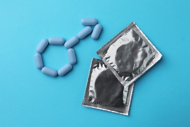 Photo of Male sign madepills and condoms on light blue background, flat lay. Potency problem