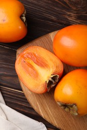 Photo of Whole and cut delicious ripe persimmons on wooden table, top view