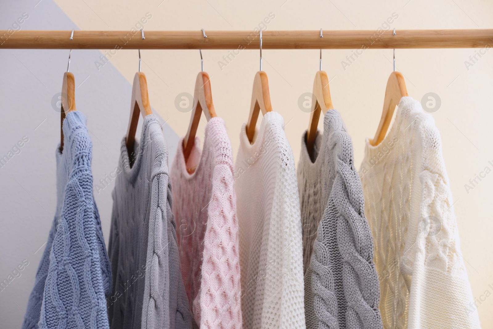 Photo of Collection of warm sweaters hanging on rack near color wall, closeup