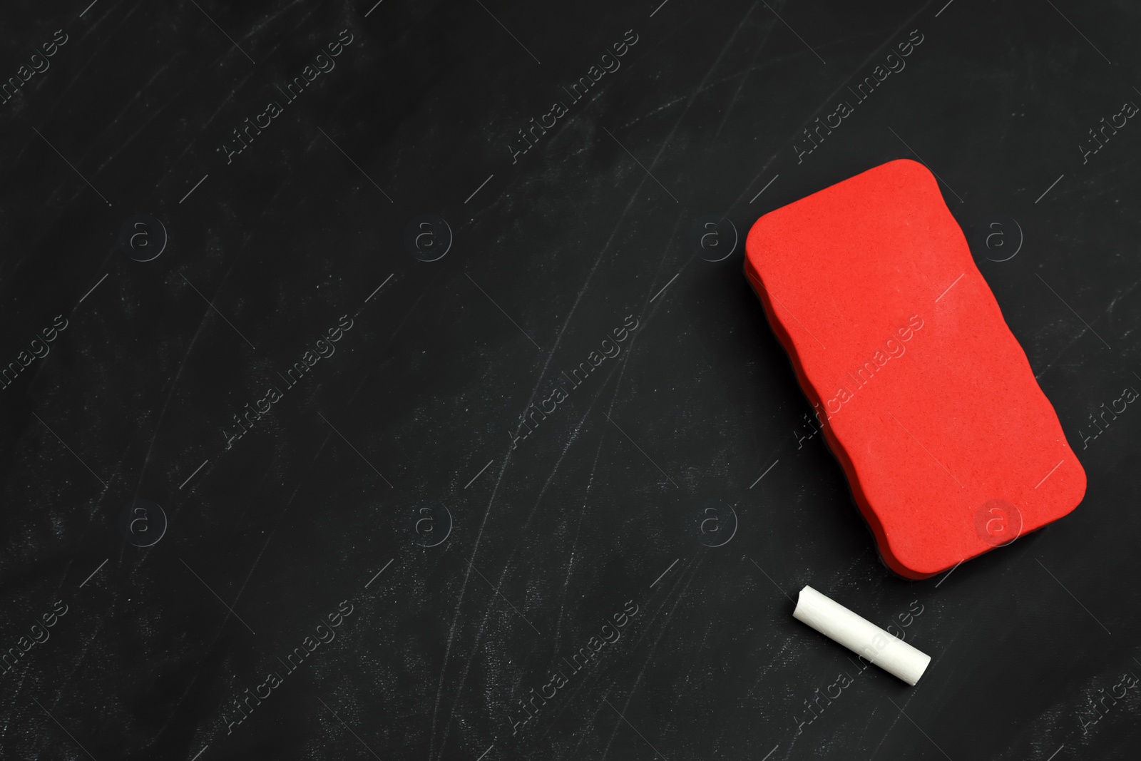 Photo of White chalk and duster on black board, flat lay. Space for text