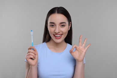 Photo of Happy young woman holding plastic toothbrush and showing OK gesture on light grey background