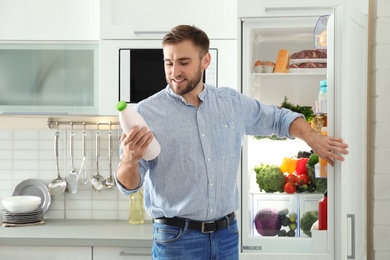 Photo of Man taking bottle with milk out of refrigerator in kitchen