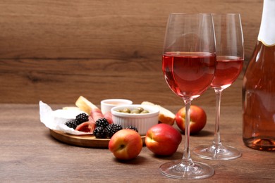 Delicious rose wine and snacks on wooden table. Space for text