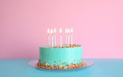 Fresh delicious birthday cake with candles on table against color background