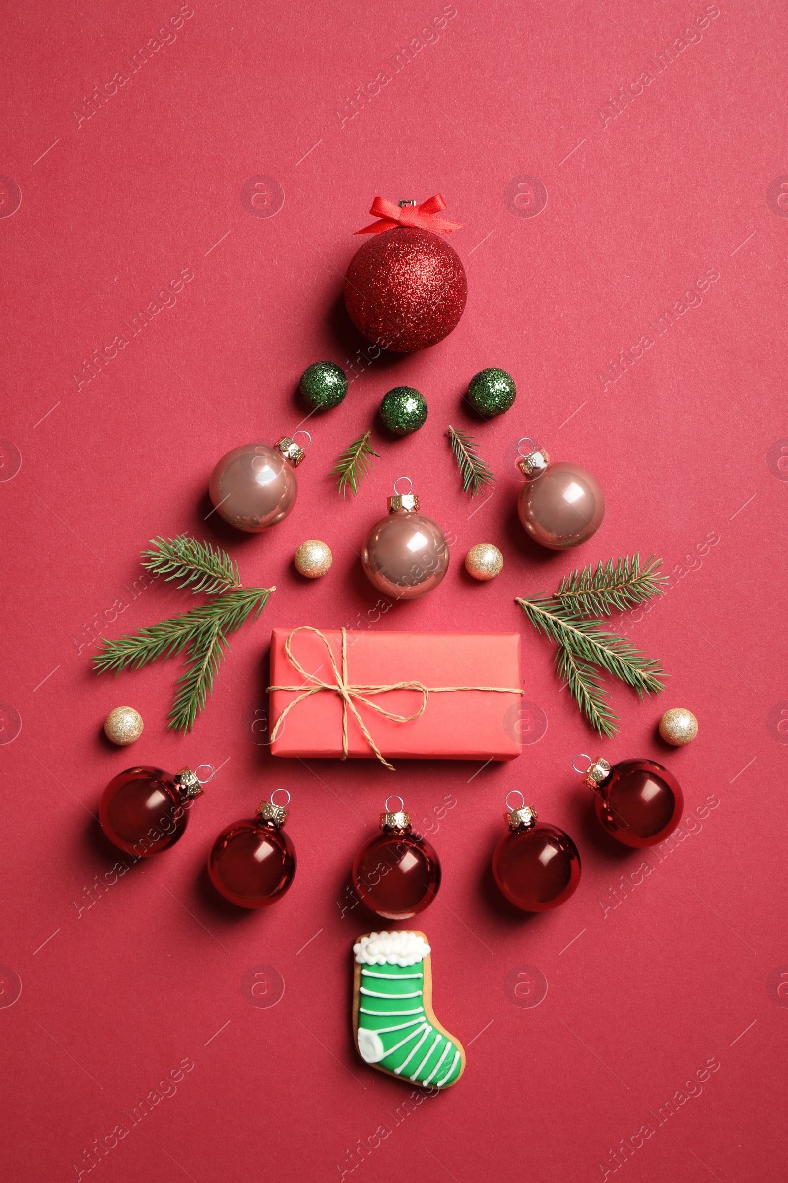 Photo of Christmas tree silhouette of fir branches and festive decoration on red background, flat lay