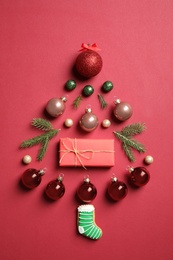 Photo of Christmas tree silhouette of fir branches and festive decoration on red background, flat lay