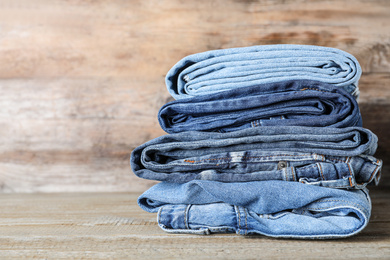 Stack of different jeans on wooden table. Space for text