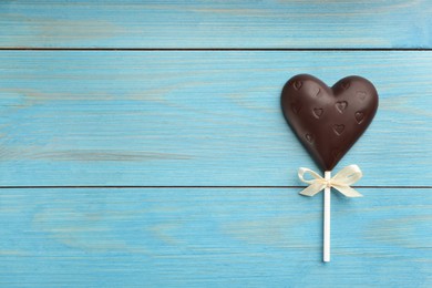 Photo of Chocolate heart shaped lollipop on turquoise wooden table, top view. Space for text