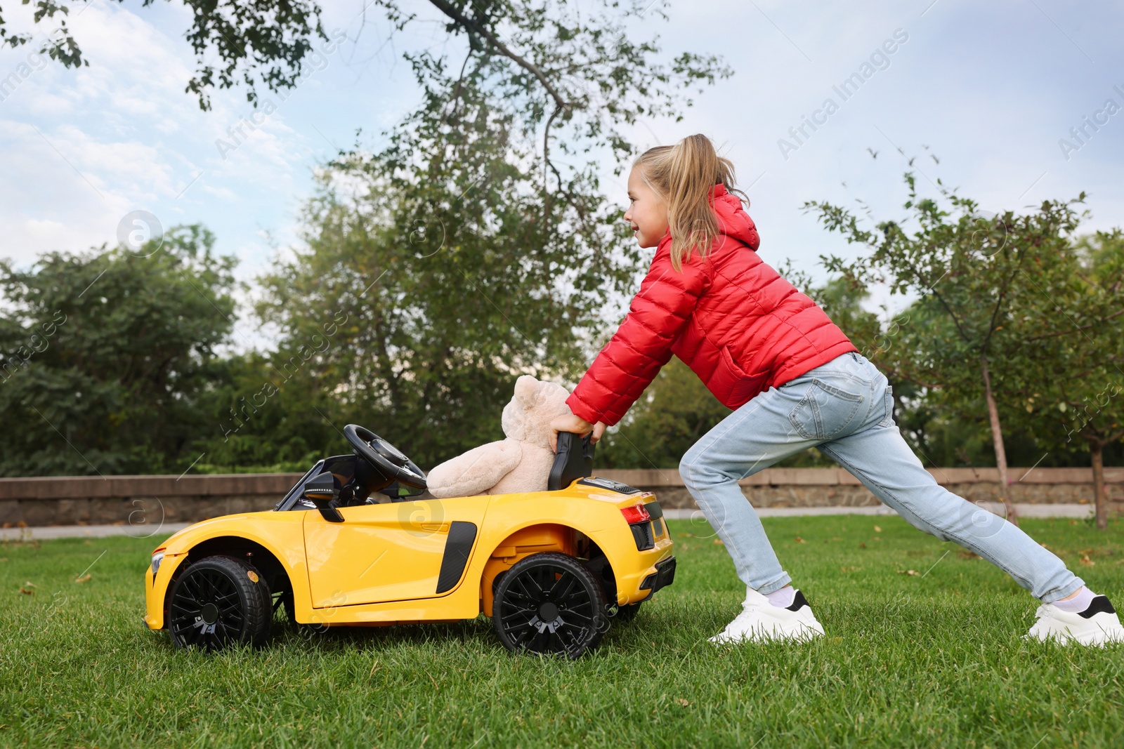 Photo of Cute little girl playing with toy bear and children's car in park