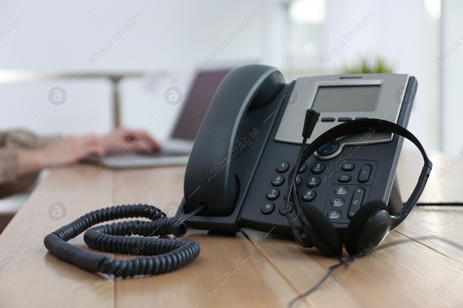 Photo of Desktop telephone with headset on wooden table in office. Hotline service