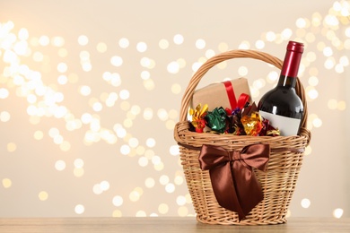 Wicker basket with gifts, wine and food against blurred festive lights. Space for text