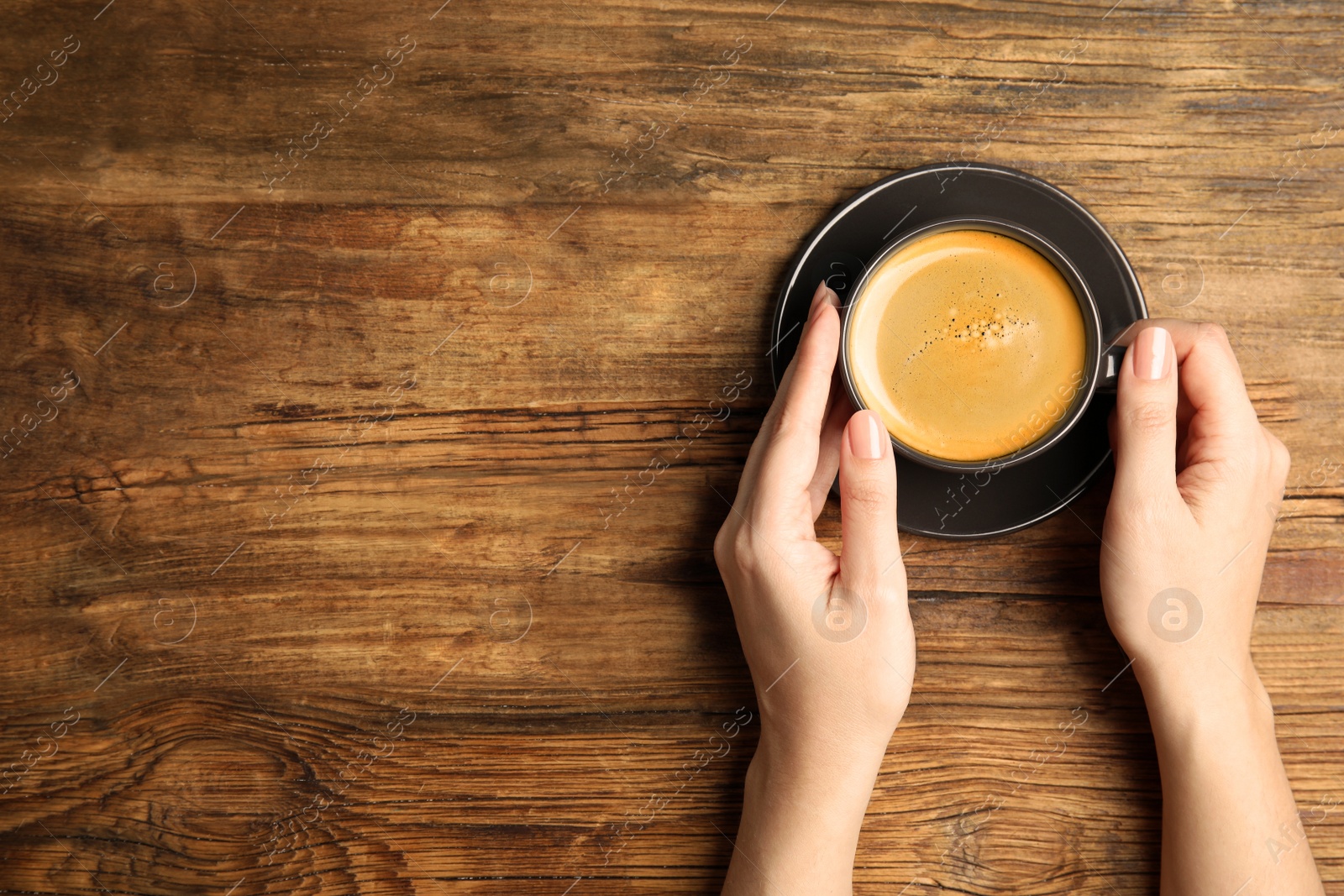 Photo of Woman with cup of coffee at wooden table, top view. Space for text