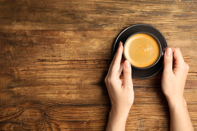 Photo of Woman with cup of coffee at wooden table, top view. Space for text