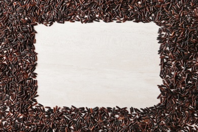 Frame made with black rice on white wooden background, top view. Space for text