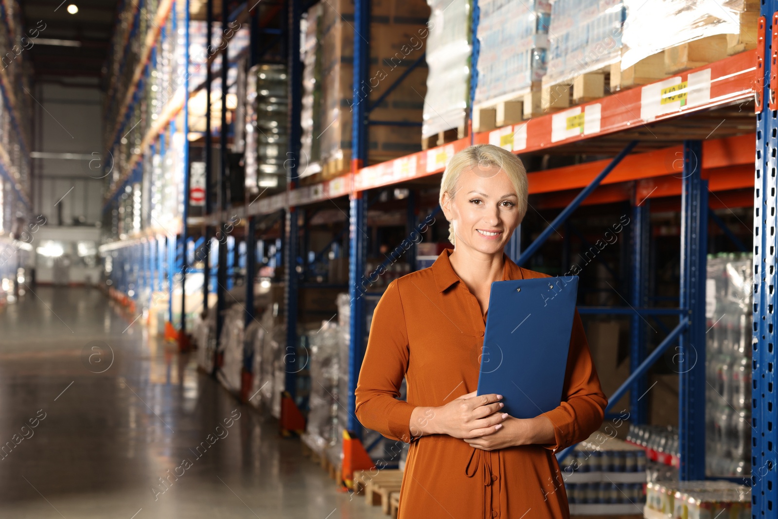 Photo of Happy manager holding clipboard in warehouse with lotsproducts. Space for text