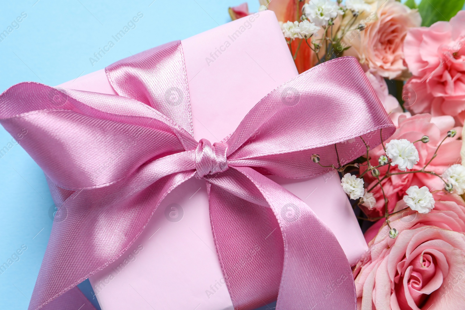 Photo of Gift box and beautiful flowers on light blue background, closeup