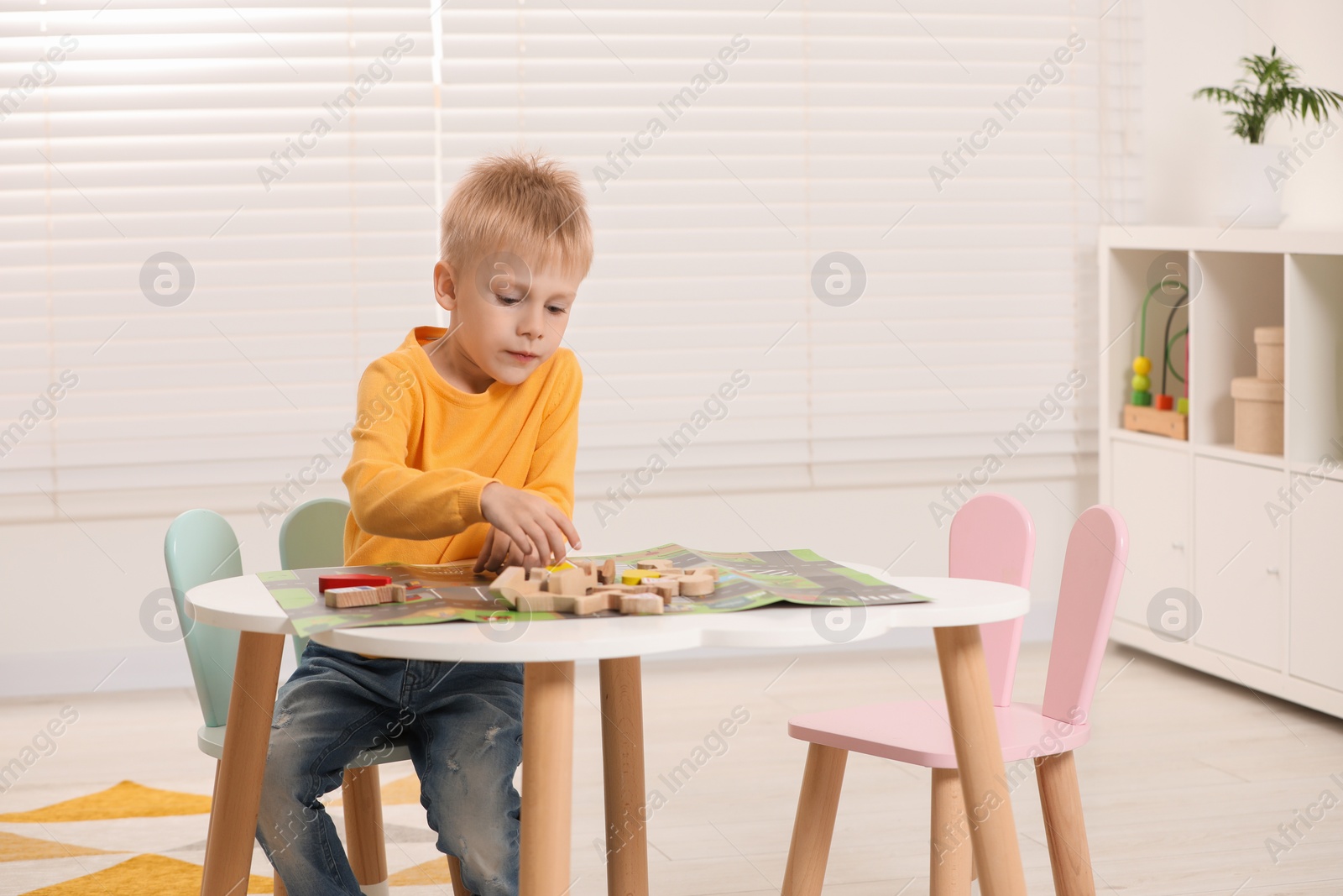 Photo of Cute little boy playing with set of wooden road signs and cars at table indoors, space for text. Child's toy