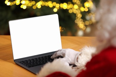 Merry Christmas. Santa Claus using laptop at table against blurred lights, closeup