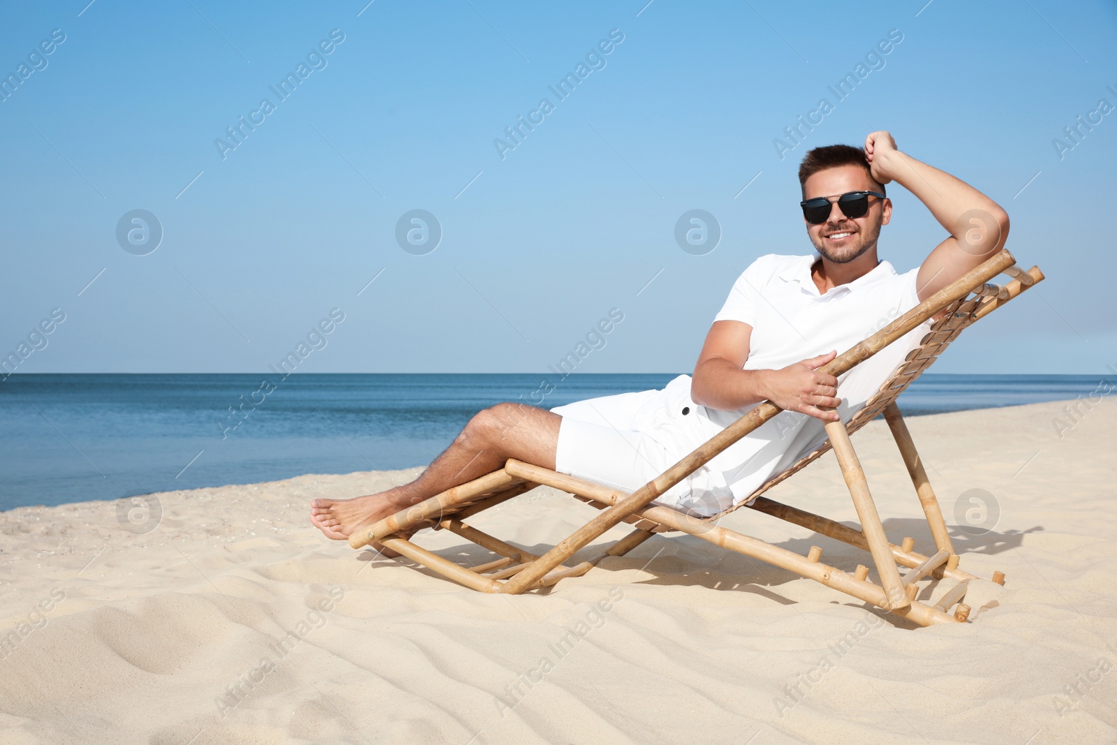 Photo of Young man relaxing in deck chair on sandy beach