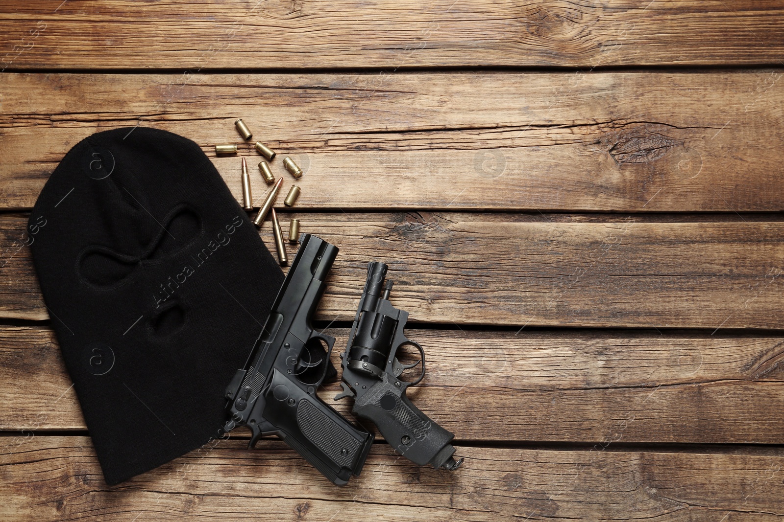 Photo of Balaclava, pistols and bullets on wooden table, flat lay. Space for text