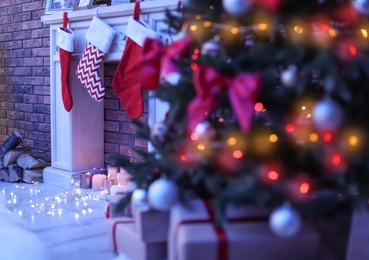 Photo of Decorative fireplace with red stockings near Christmas tree in dark room