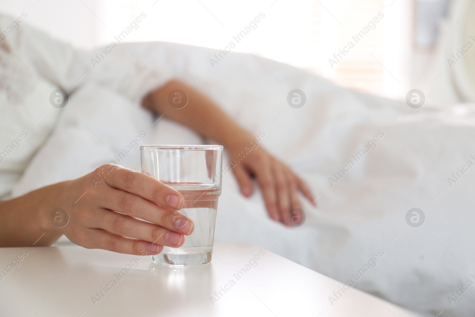 Photo of Woman taking glass of water from nightstand in bedroom, closeup