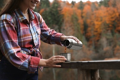 Woman pouring hot drink from metallic thermos into cup lid outdoors, closeup. Space for text