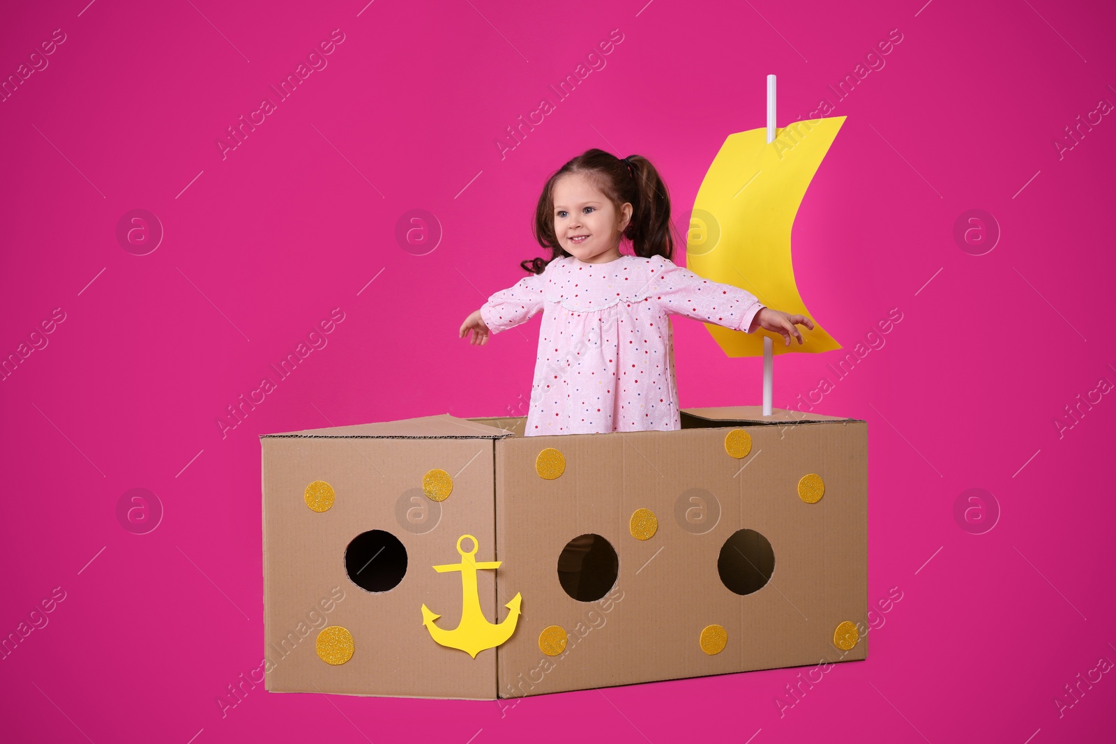 Photo of Little child playing with ship made of cardboard box on pink background