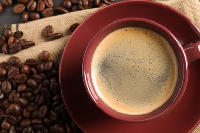 Cup of hot aromatic coffee and roasted beans on black table, flat lay. Space for text