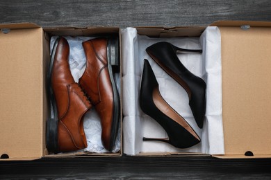 Photo of Stylish men's and women's shoes in cardboard boxes on wooden floor, flat lay
