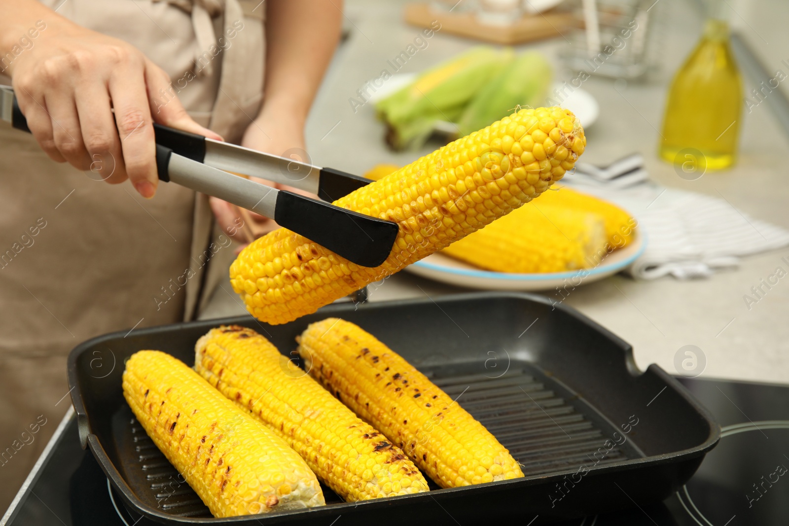 Photo of Woman cooking fresh corn cobs on grill pan, closeup