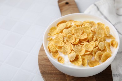 Photo of Breakfast cereal. Tasty corn flakes with milk in bowl on white tiled table, closeup. Space for text