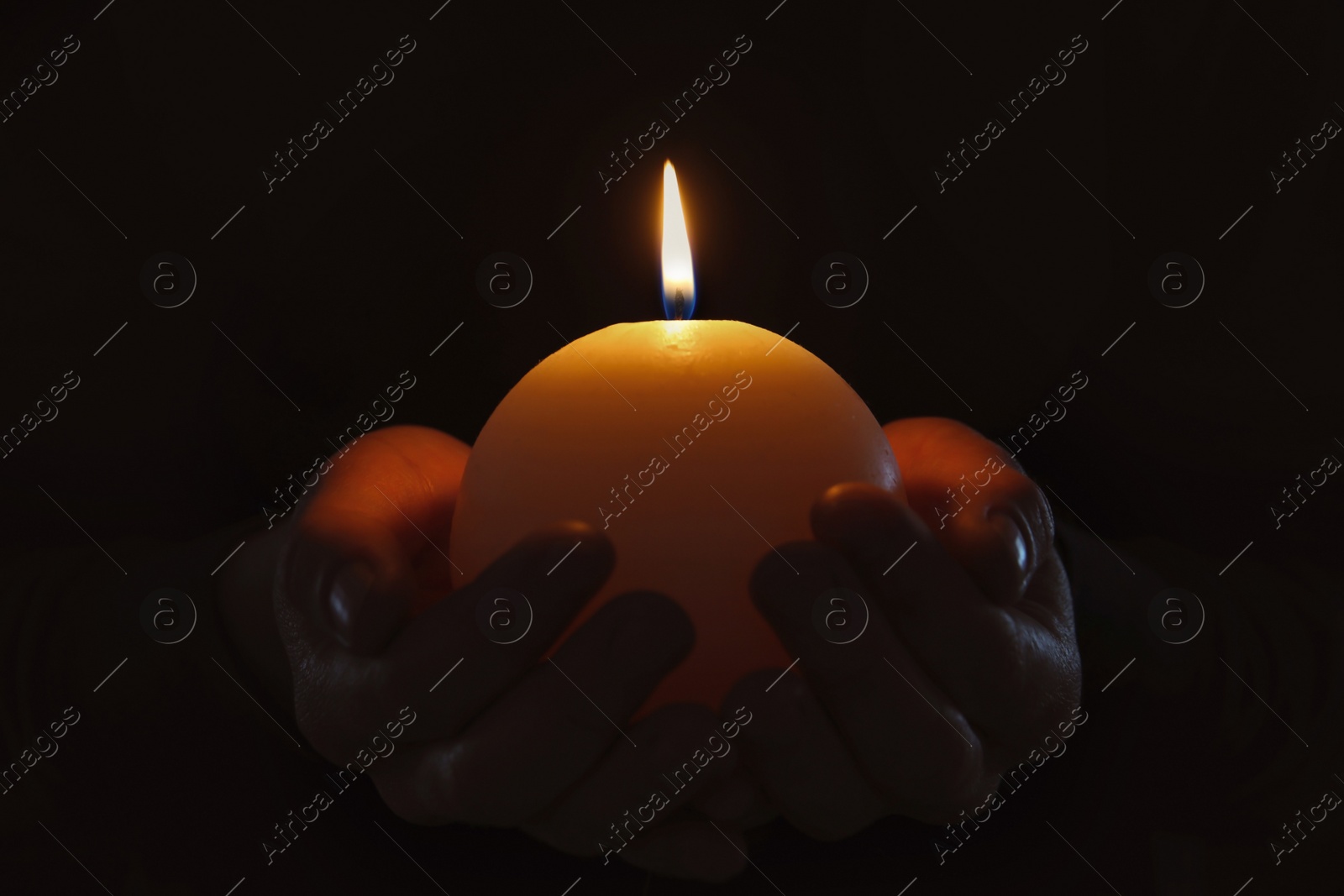 Photo of Young person holding burning candle in darkness, closeup