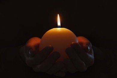 Photo of Young person holding burning candle in darkness, closeup