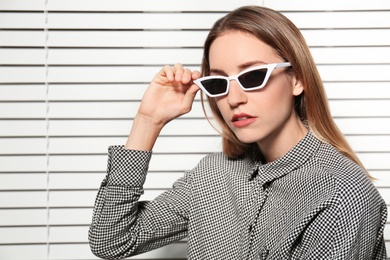 Photo of Young woman wearing stylish sunglasses against blinds