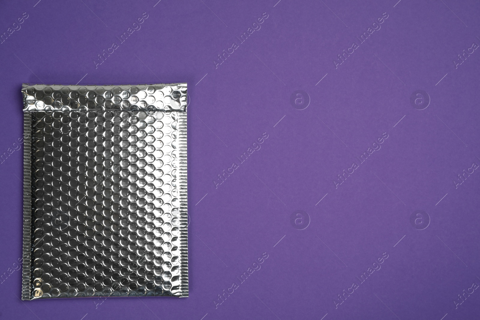 Photo of Padded envelope with bubble wrap on purple background, top view. Space for text