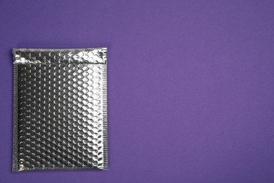 Photo of Padded envelope with bubble wrap on purple background, top view. Space for text