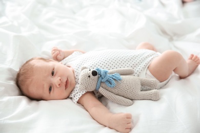 Photo of Adorable newborn baby with toy lying on bed sheet