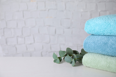 Photo of Stack of clean bath towels and green branch near textured wall. Space for text