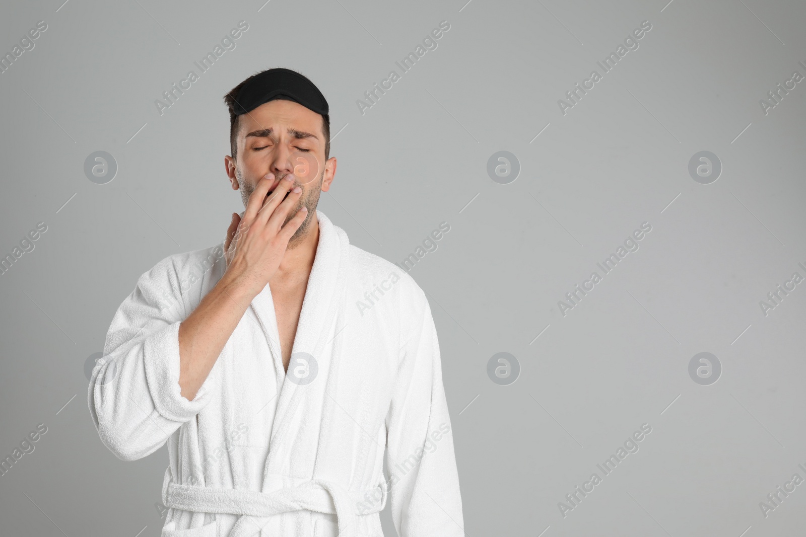 Photo of Sleepy young man in bathrobe on light grey background. Space for text