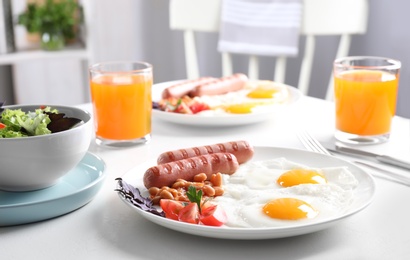 Delicious breakfast with fried eggs and sausages served on white table