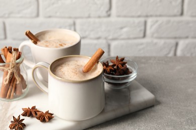 Photo of Cups of delicious eggnog with anise and cinnamon on light grey table. Space for text