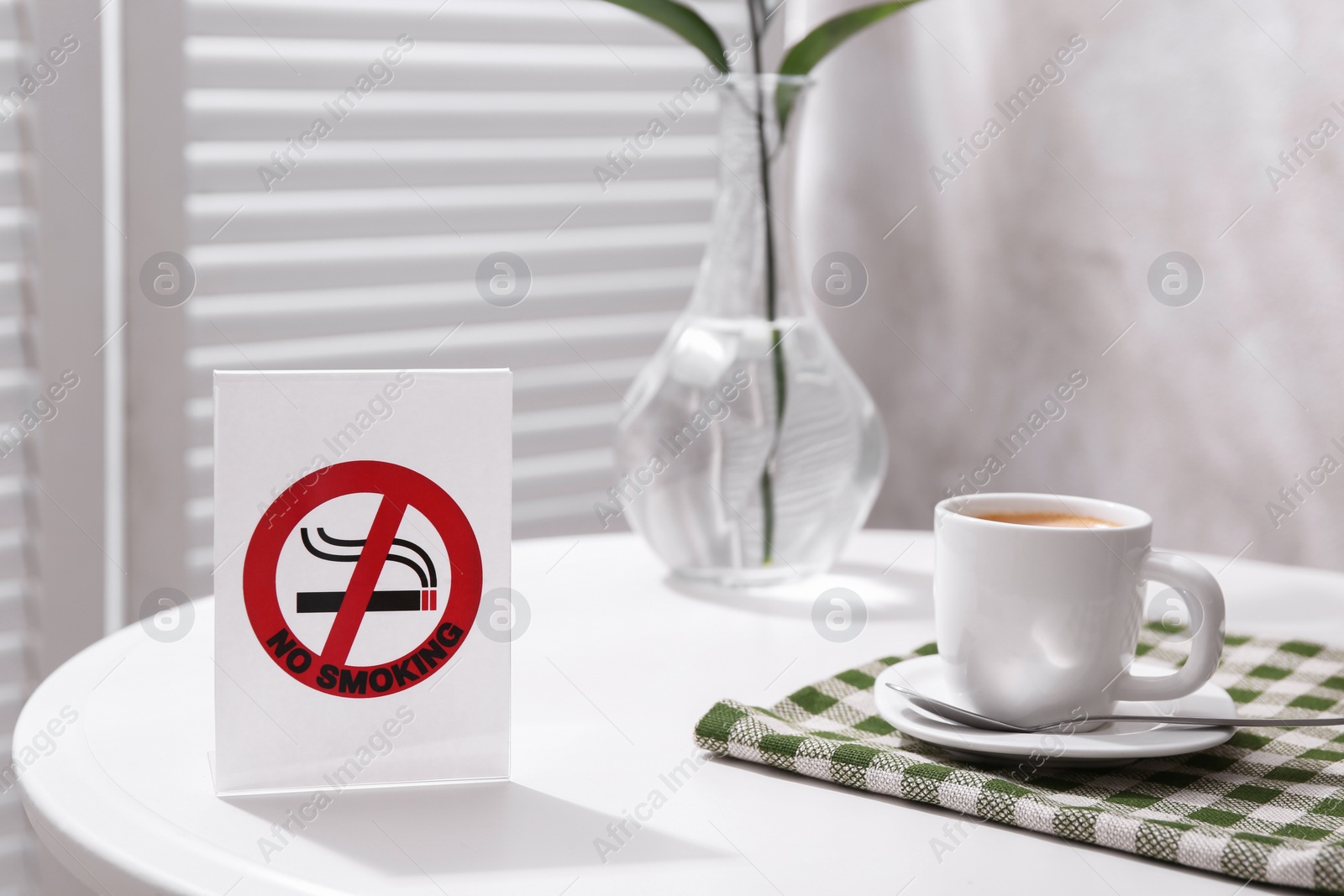 Photo of No Smoking sign and cup of coffee on white table indoors