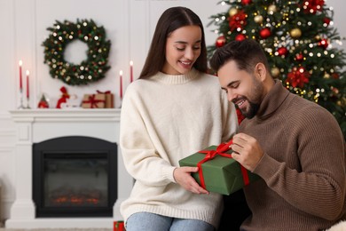 Photo of Happy young man opening Christmas gift from his girlfriend at home