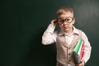 Photo of Cute little child wearing glasses near chalkboard, space for text. First time at school